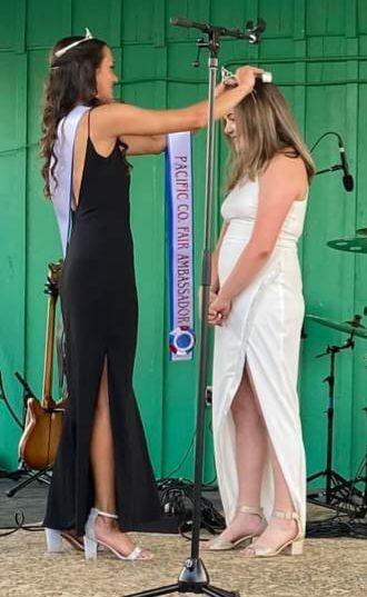 A woman in a black dress is crowning another woman in a white dress.