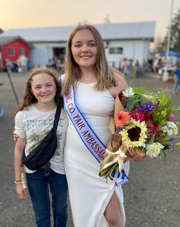 A woman in a white dress is holding a bouquet of flowers next to a young girl.