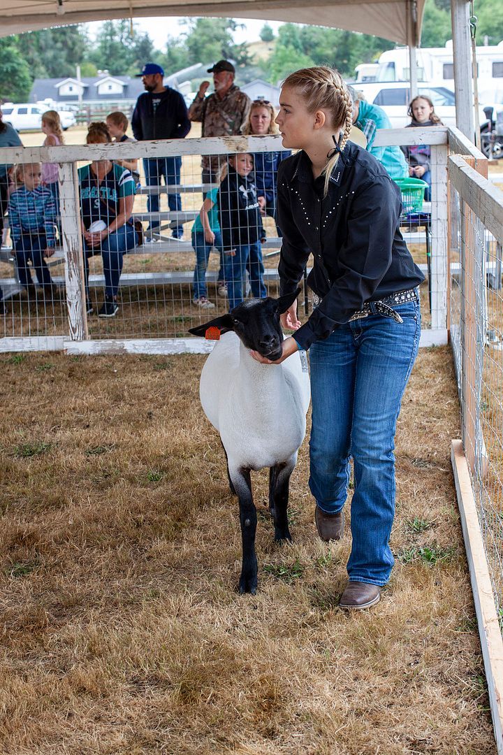 A woman is holding a sheep in a pen at a fair.