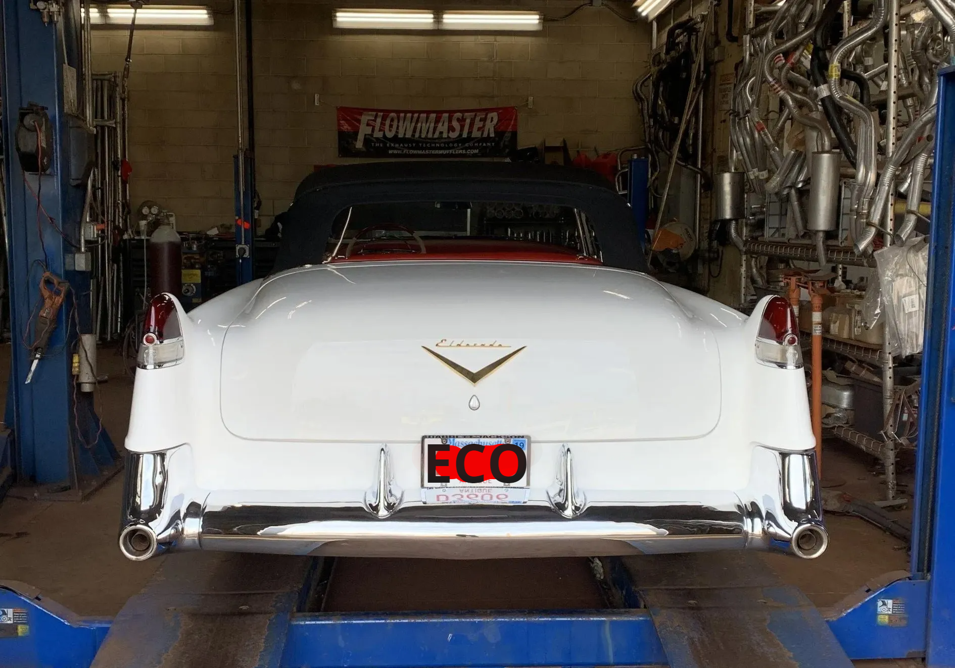 A white cadillac is sitting on a lift in a garage.