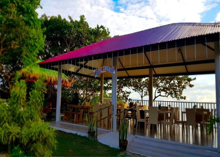 Open-air dining structure with pink and purple roof overlooking a landscape. Tables and chairs are inside.