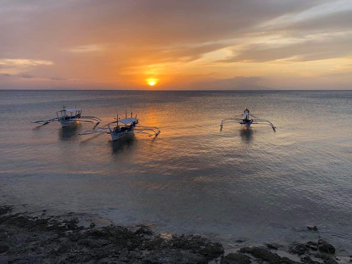 Sunset over calm ocean with three boats, water reflecting golden light.