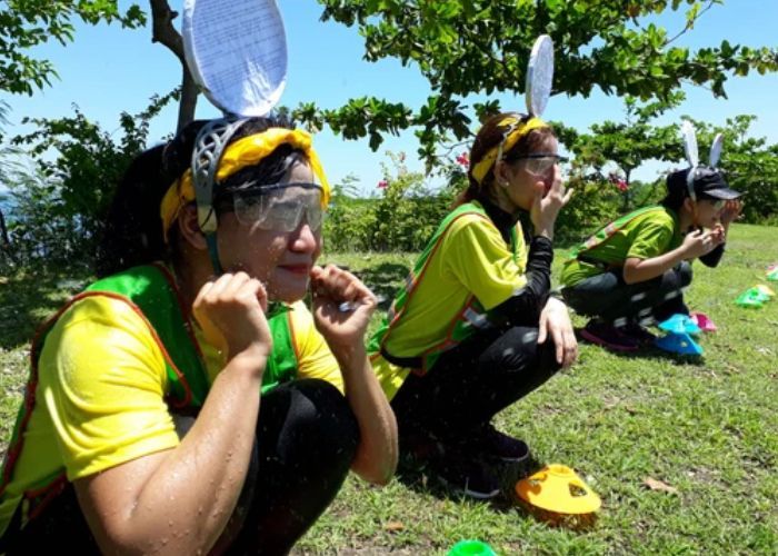 Three people in bunny ear headbands and goggles squatting on grass, looking focused.
