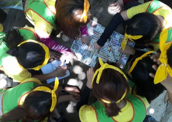 Group of people in green and yellow shirts, heads together, looking at a map and writing.