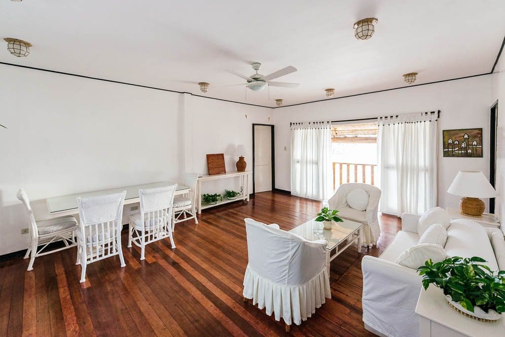 Bright white living room with hardwood floors and white furniture. Large glass doors lead to a balcony.