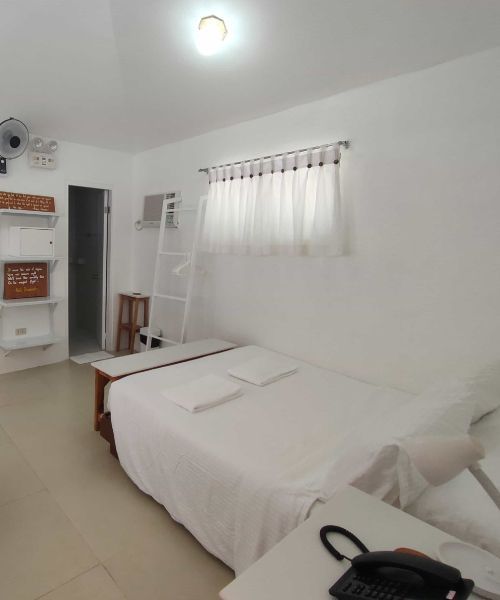White bedroom with a bed, small window, and shelves.