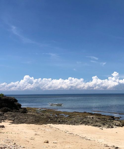 Sandy beach meets calm blue ocean under a bright, partly cloudy sky.