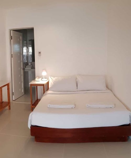 Bedroom with a bed, nightstand, and doorway to a bathroom. White walls, bed linens, and towels.