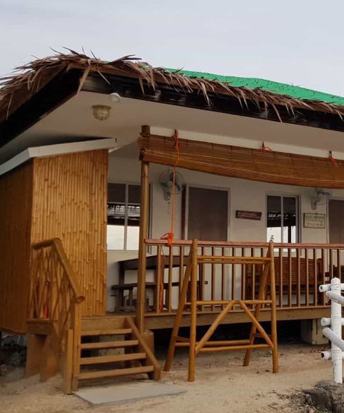 Bungalow with thatched roof and bamboo siding, wooden deck with stairs.