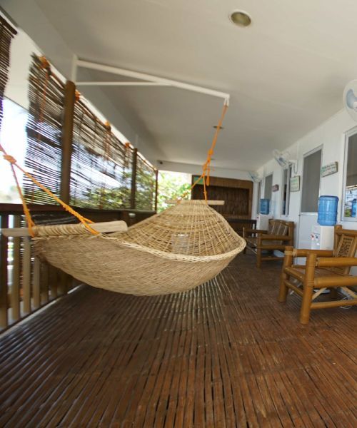 Woven hammock hangs on a bamboo veranda, with bamboo furniture and water dispensers visible.