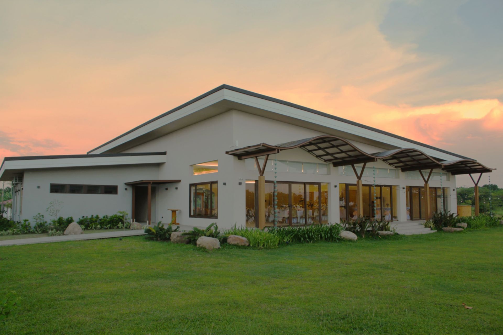 A white building with large windows is set on a grassy lawn under a sunset sky.