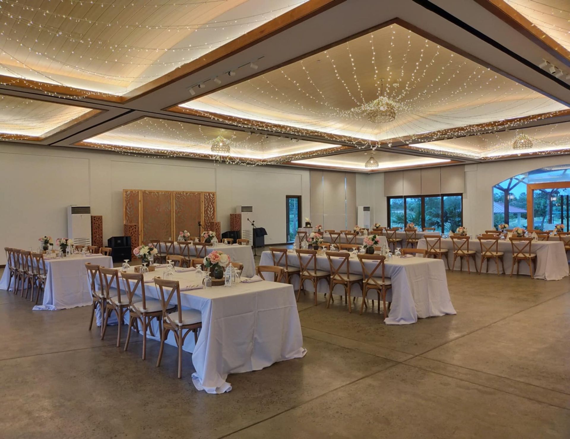 Banquet hall with tables set for an event, soft lighting, and cross-back chairs.