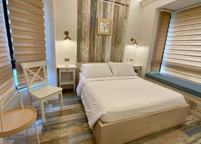 Bedroom with a double bed, bedside tables, two sconces, a chair, and window blinds.