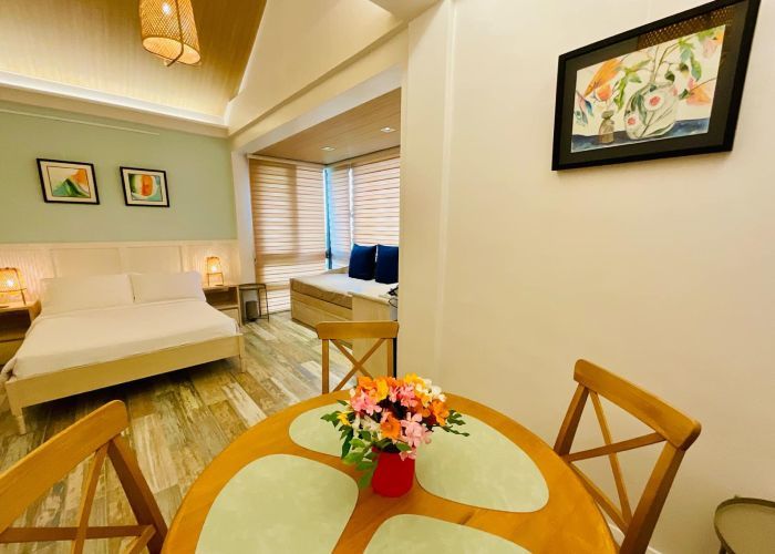 Cozy studio apartment with bedroom, living area, and dining table, decorated with art and flowers.