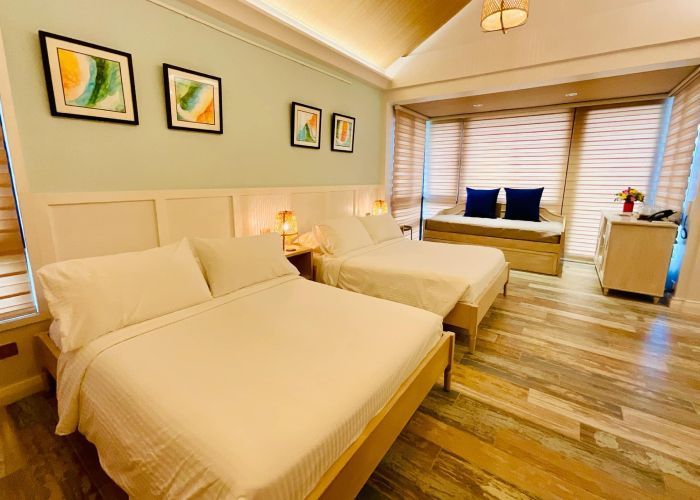 A light-filled hotel room with two beds, a seating nook, and colorful wall art.