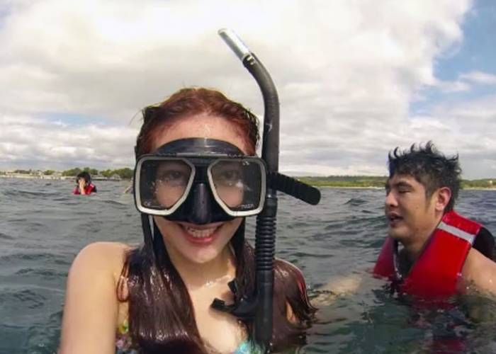 Woman with snorkel and mask in water, smiling at camera. Another person in background.