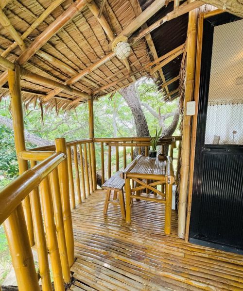 Bamboo balcony with table and bench under a thatched roof.