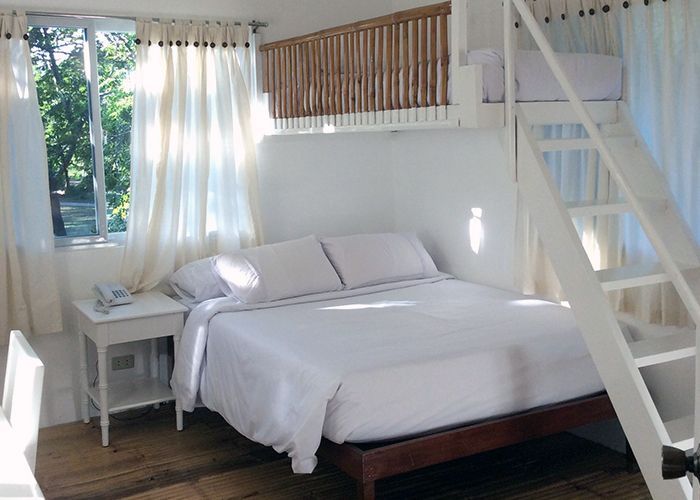 Bedroom with a white bed, curtains, and a window. A loft bed and stairs are visible.