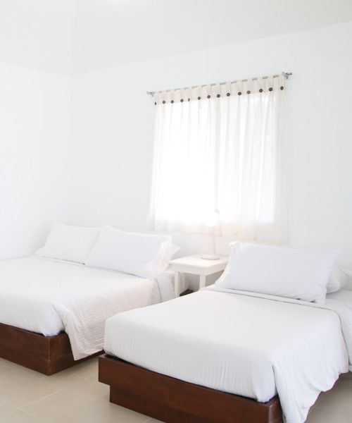 White bedroom with two beds and a window with white curtains.