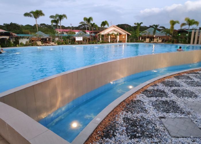Swimming pool with clear blue water and cabanas under cloudy sky.