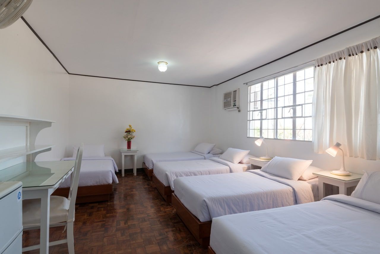 Bright, white bedroom with five beds, a desk, a window, and wooden floors.
