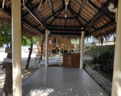 Gazebo on a beach with a thatched roof, concrete floor, and wood furniture.