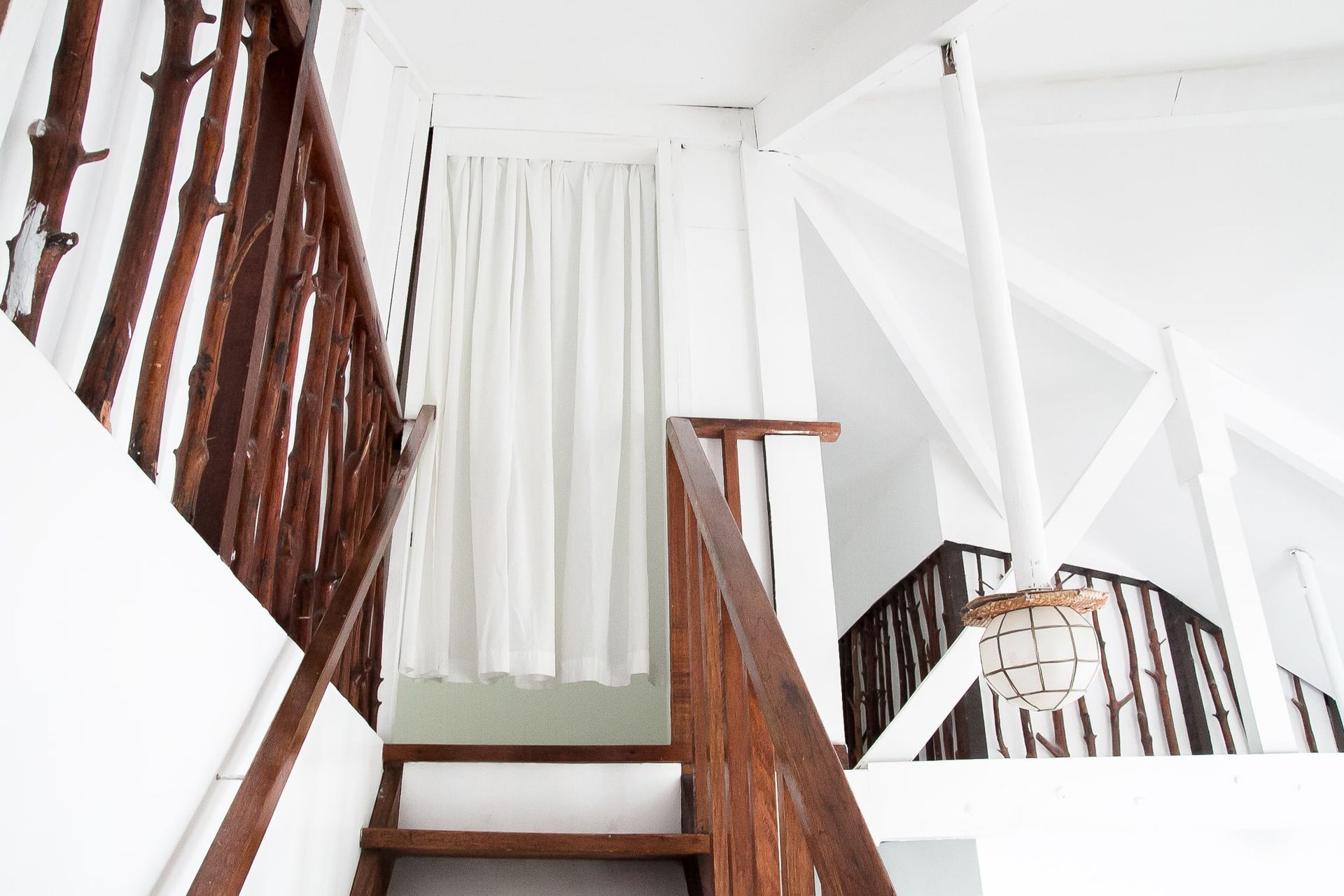 Wooden staircase with white interior, curtained doorway, and an overhead light.