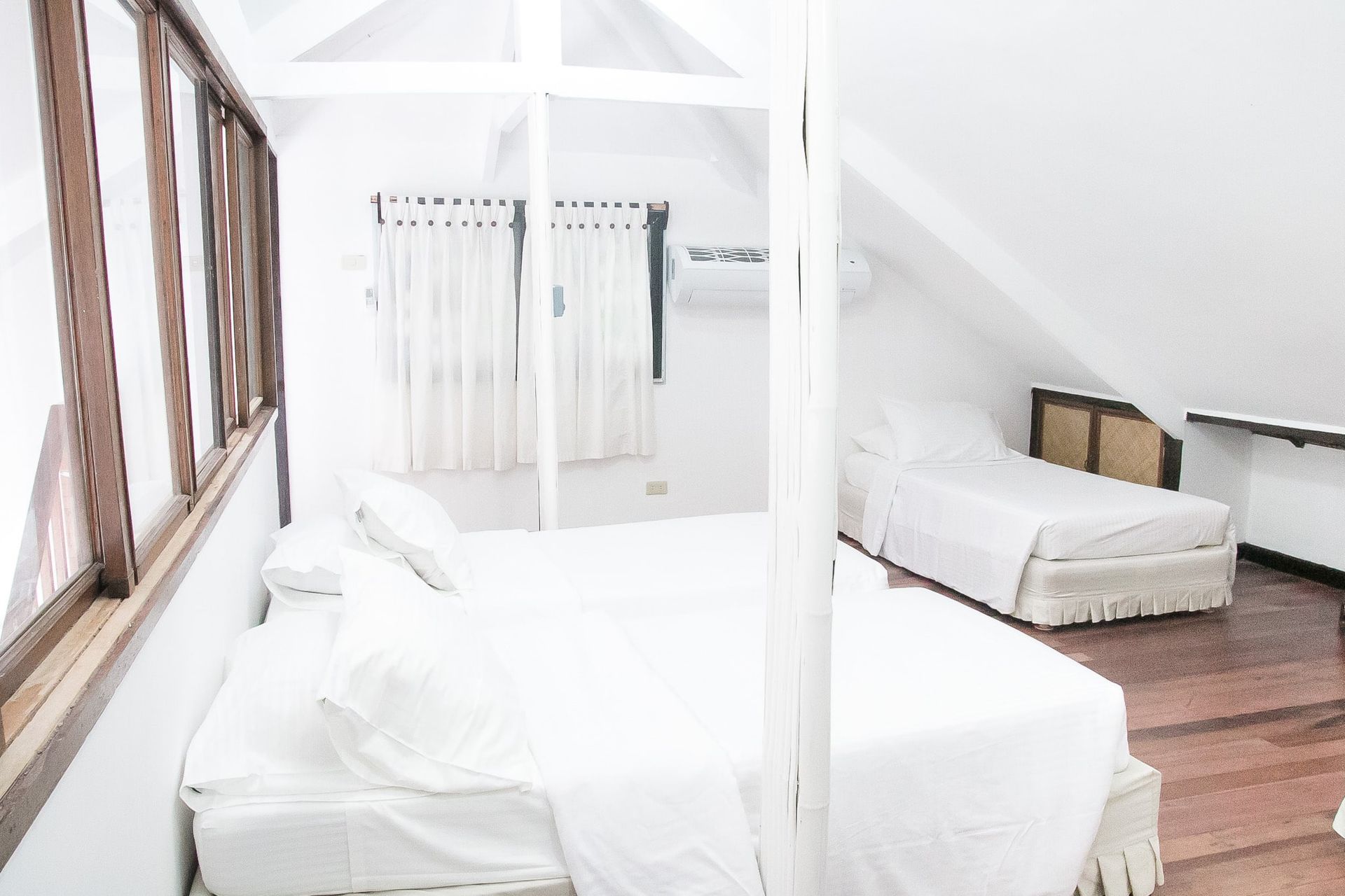 Bedroom with two white beds, window with wooden frame, and sloped ceiling.