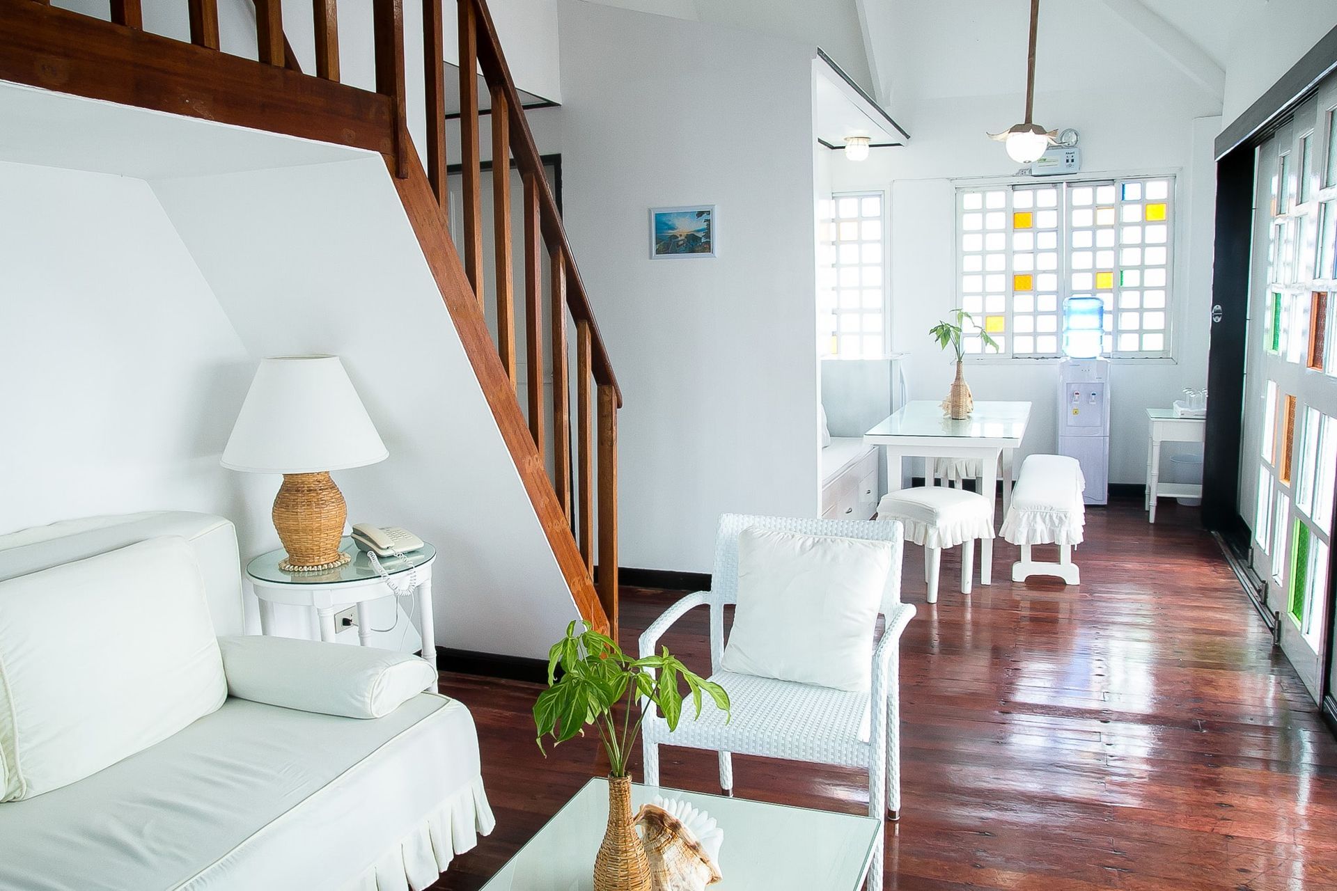 Bright, white interior with wood staircase and floors. White furniture, dining table, and large window with stained glass.