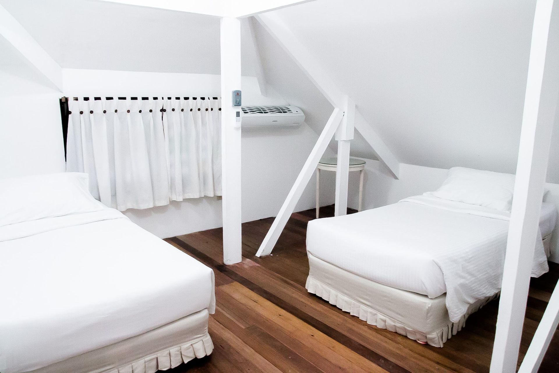 White bedroom with two beds, wooden floor, and sloped ceiling.