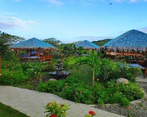 Landscaped garden with thatched-roof cabanas and a fountain under a blue sky.