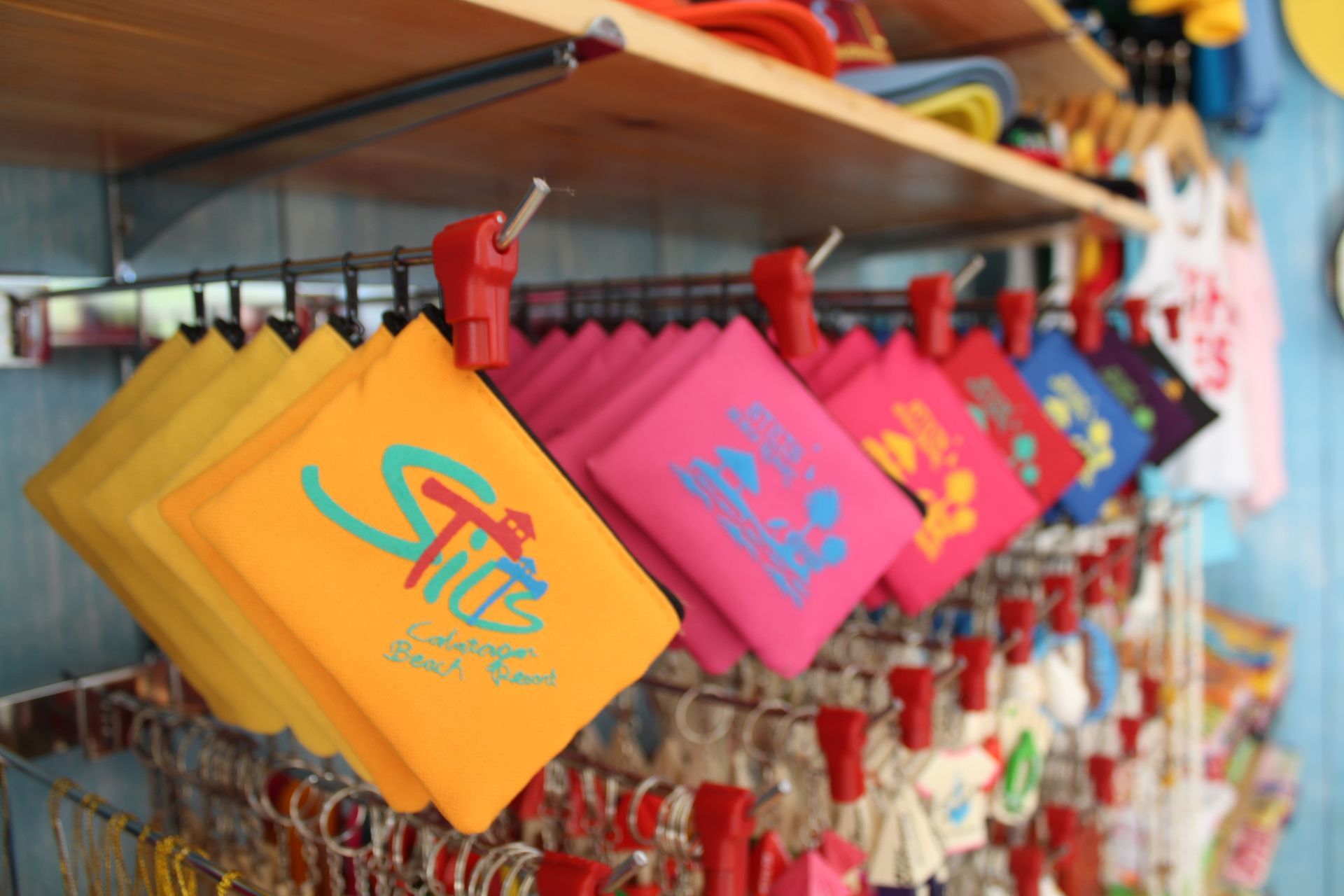 Colorful souvenir pouches displayed on a rack; yellow, pink, and red hues with printed logos.