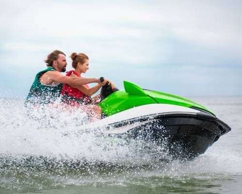 Man and woman on a green and black jet ski speeding across water, creating spray.