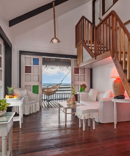Living room with white furniture, wooden stairs, and a view of the ocean.