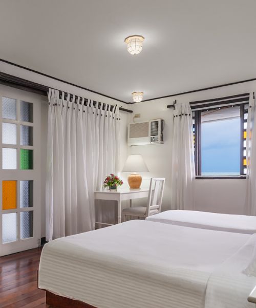 Bedroom with two white beds, white curtains, and a window with a view.