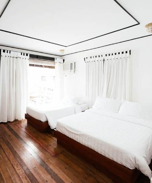 Bedroom with a large bed and a single bed; white linens, wood floor, white walls, and curtains.