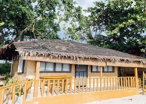Beach bungalow with thatched roof and wooden porch, near trees.