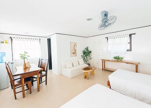 Bright white living space with dining table, sofa, two beds, and decorative plants.