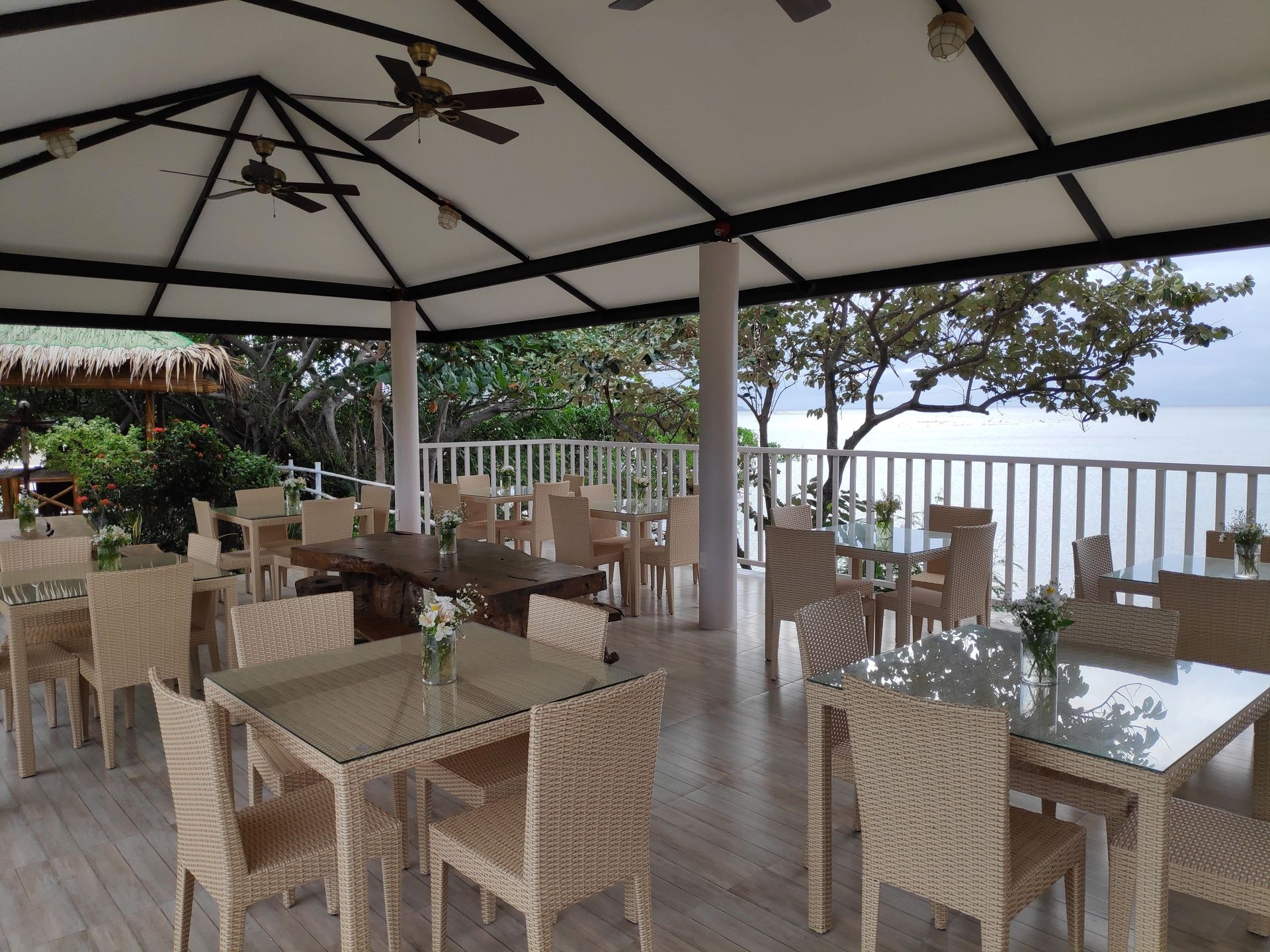 Outdoor dining area with woven chairs, glass-top tables under a white canopy overlooking the water.