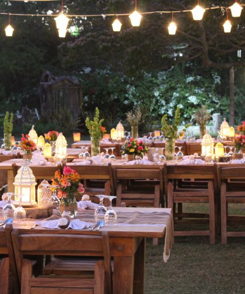 Outdoor wedding reception with wooden tables, flowers, and string lights.