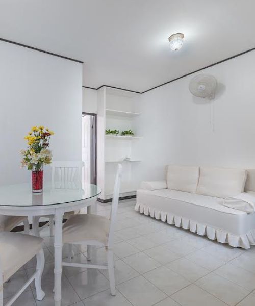 White living room with a table, chairs, sofa, and a wall fan.