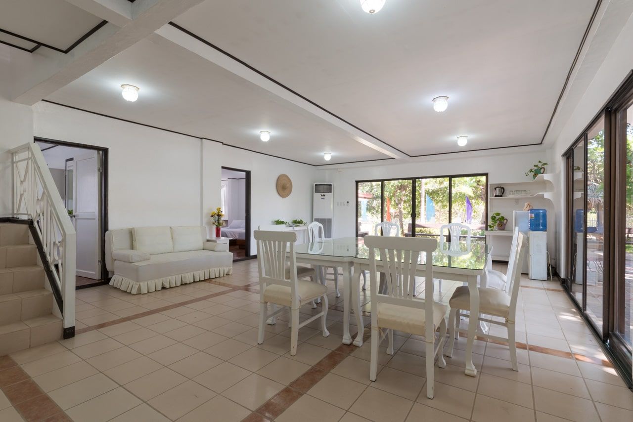 Bright dining area with white furniture, large windows, and staircase leading upwards.