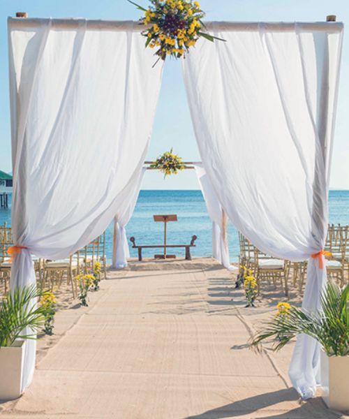 Beach wedding ceremony with white draped archway and ocean view.