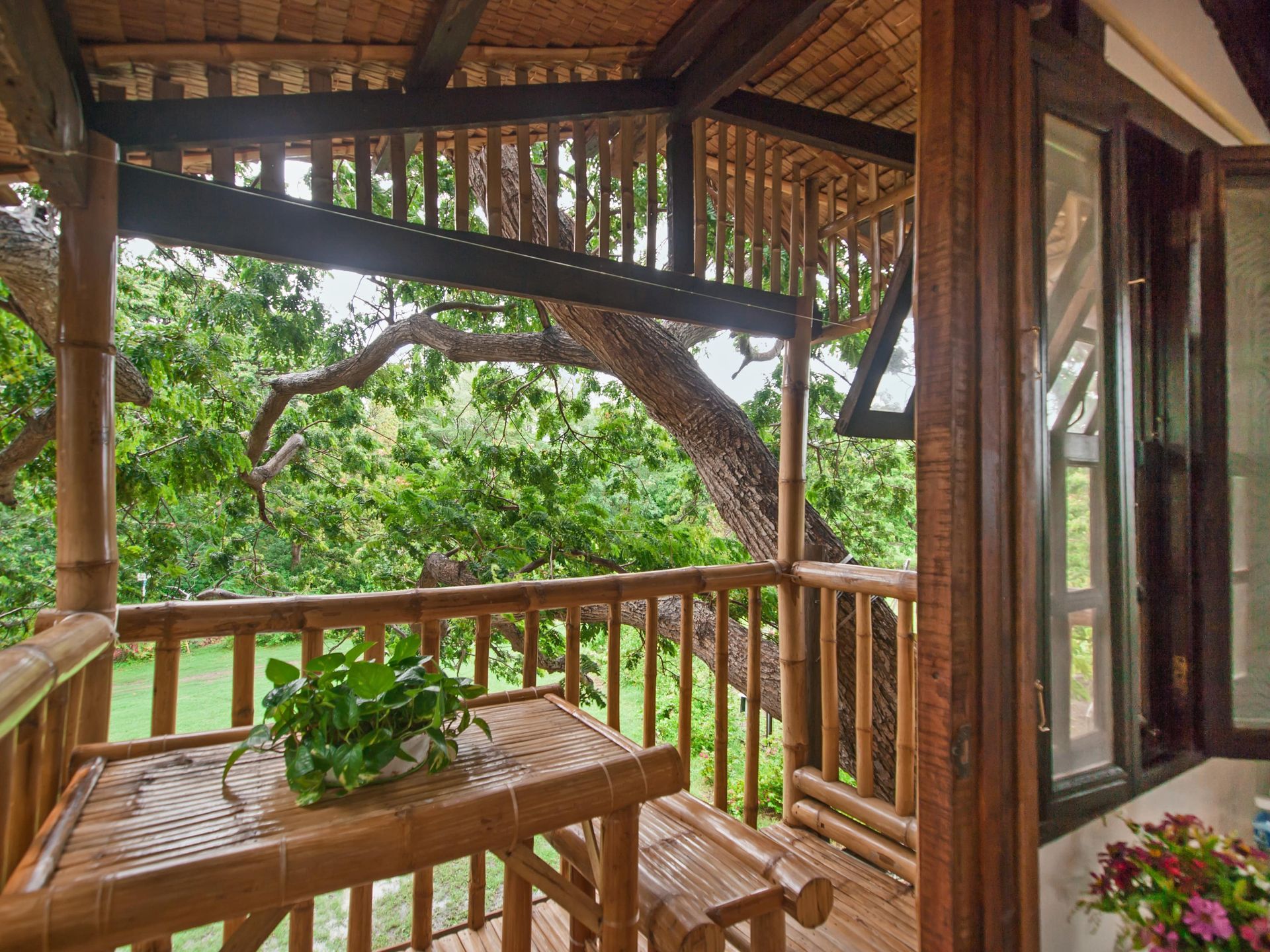 Bamboo balcony with table and bench, overlooking a lush green tree.