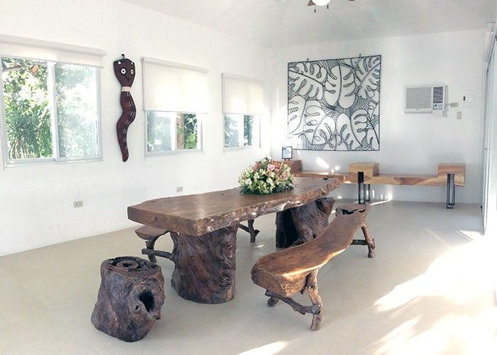 Bright, spacious room with large wooden table, benches, and wall art. Windows provide natural light.