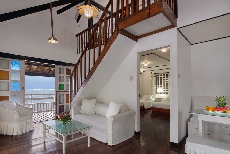 Interior of a white beach house with a staircase, a sofa, and a view of the ocean.