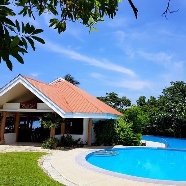 Resort building with orange roof, pool, and trees under a blue sky.