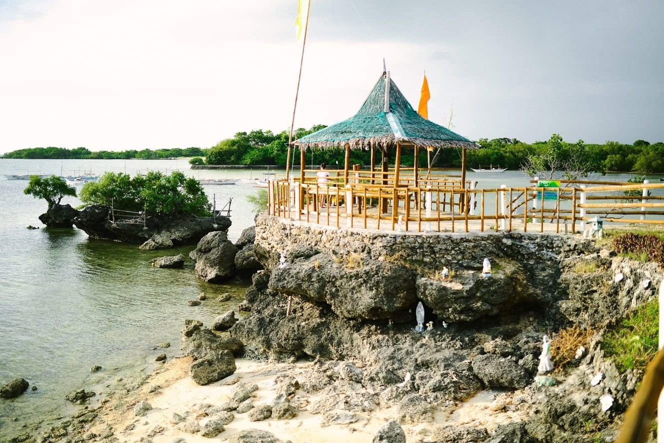Gazebo on rocky shore with a thatched roof, overlooking the water with a small island.