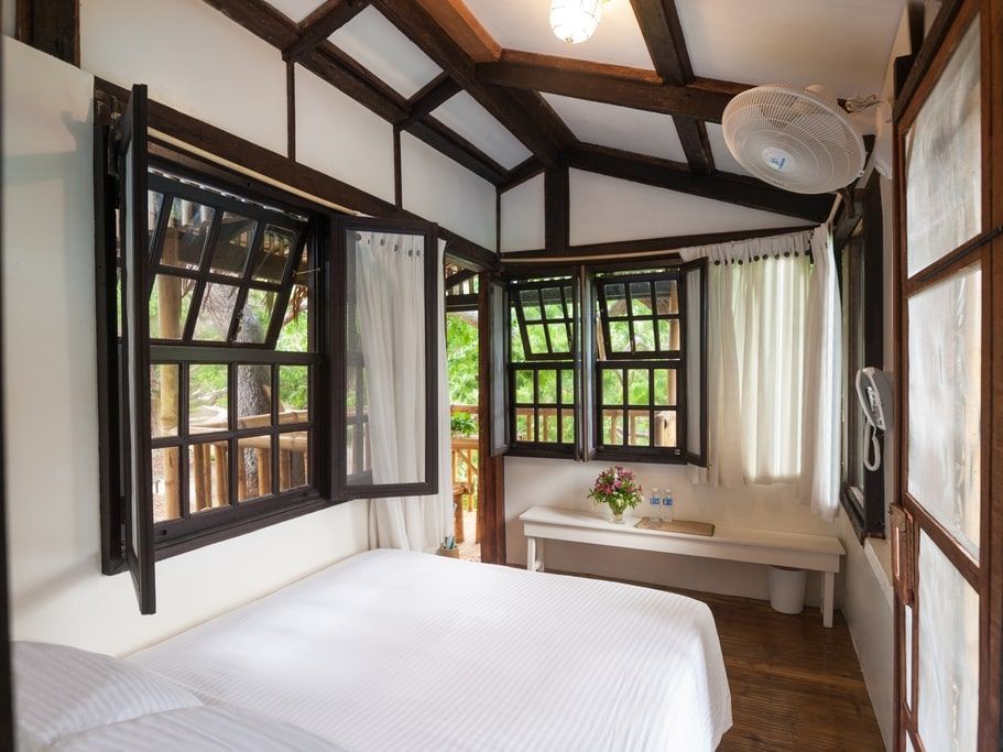 Bedroom with white bedding, wood-framed windows, and a bench under the windows.