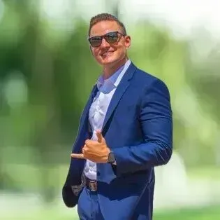 A man in a blue suit and sunglasses is giving a thumbs up.